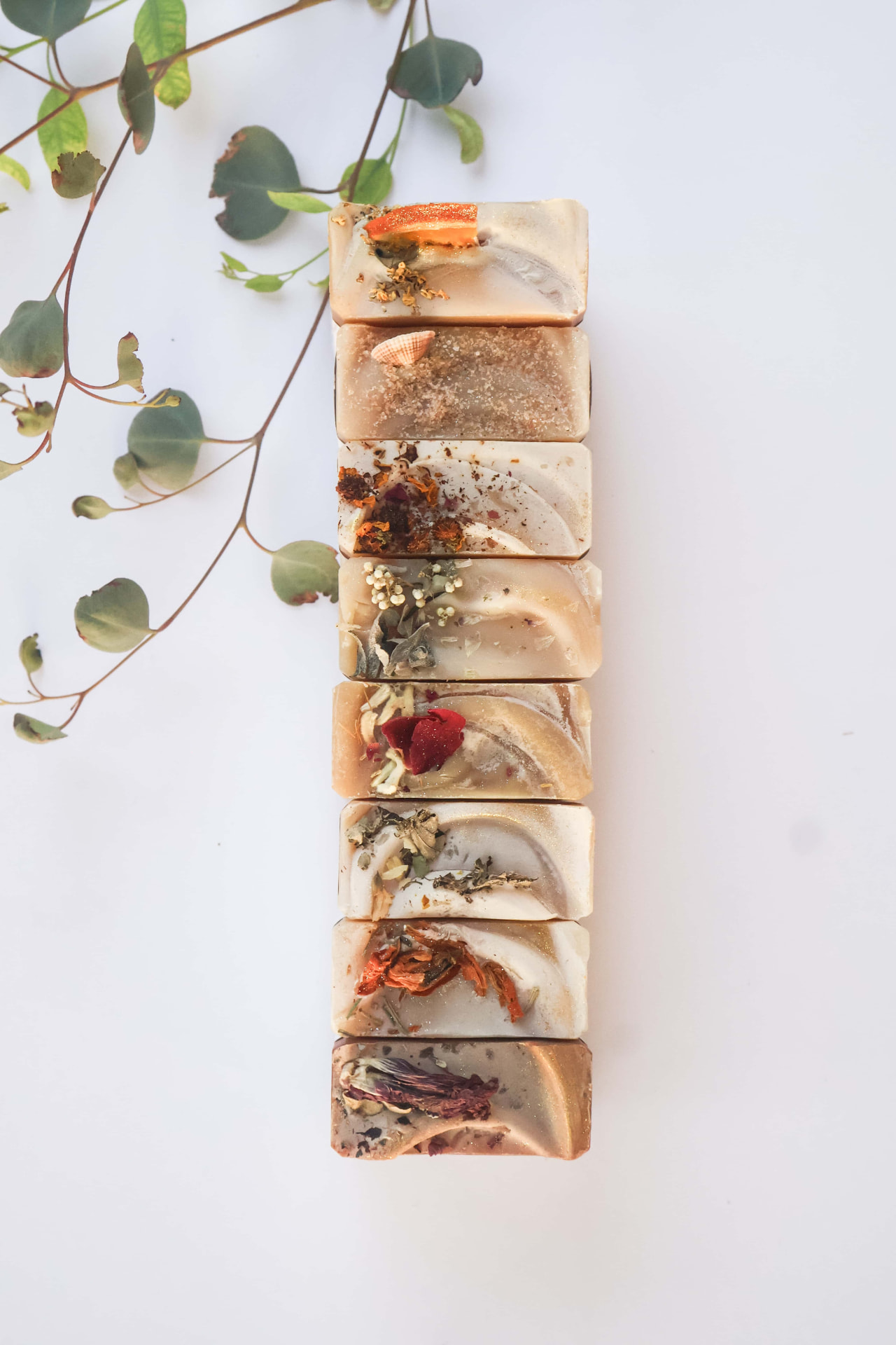 A stack of handmade tallow soaps, each topped with dried flowers, herbs and citrus